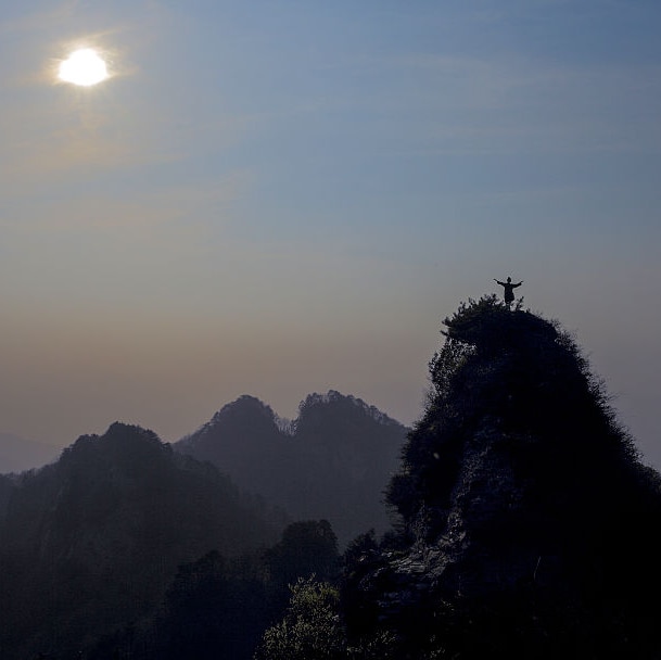 image of man standing on top of mountain ranges facing towards the sun