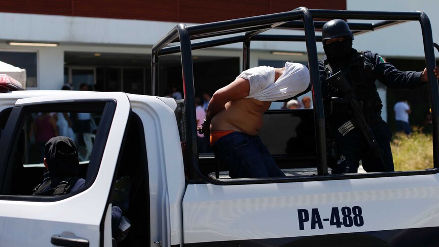 Police escort a man with a white shirt covering his head into a police vehicle.