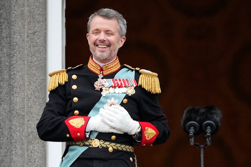 A man in military dress uniform clutches his chest and smiles