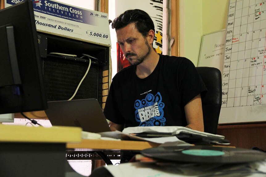 Music NT's Mark Smith sits at a desk in his office, looking at a computer screen.