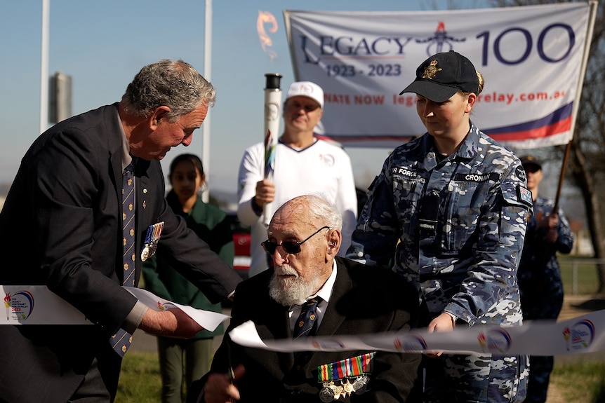 An elderly man in a wheelchair cuts the ribbon for a race.