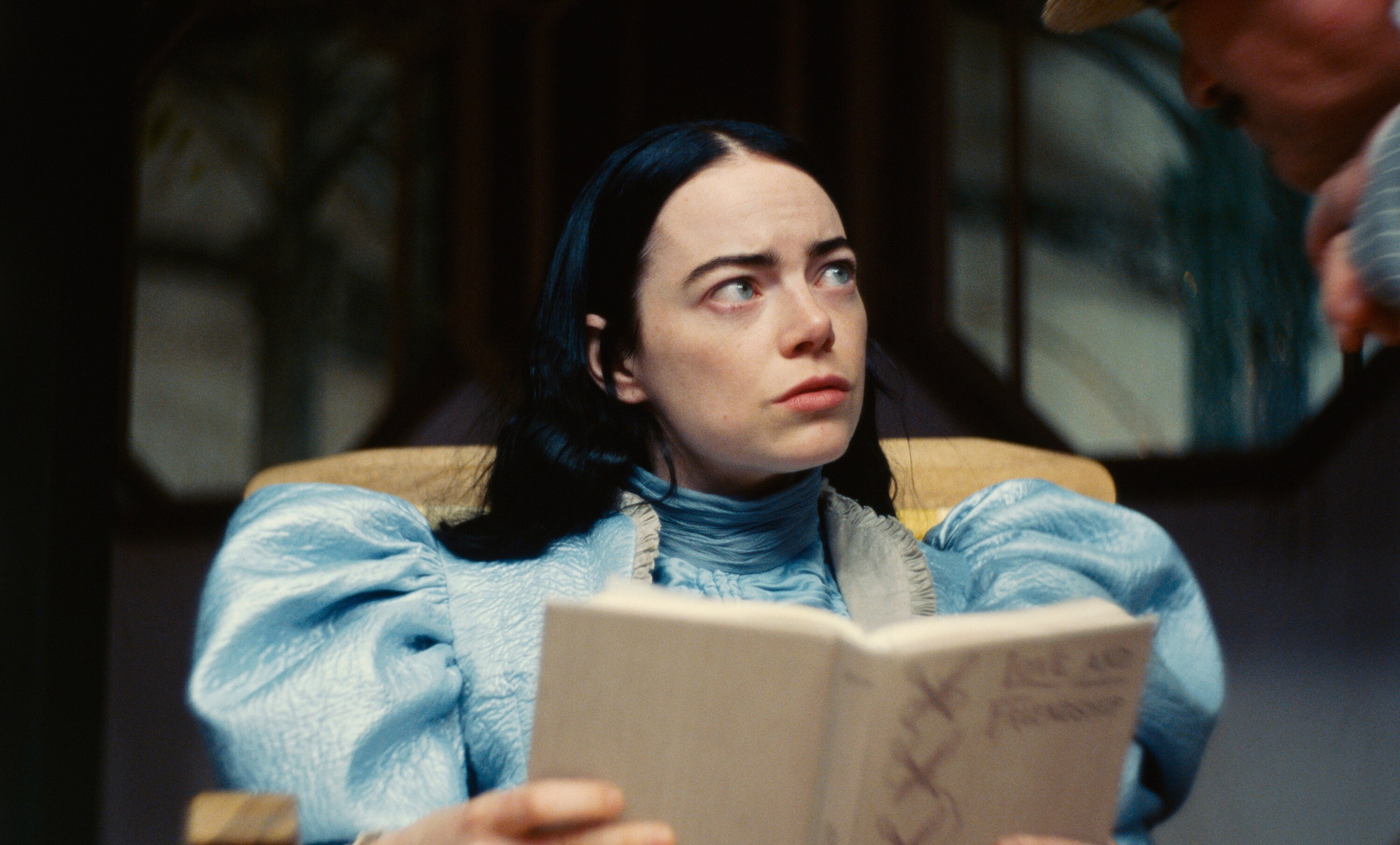 Emma Stone, as main character Bella Baxter, holds a hardcover book and looks worrying to the side.