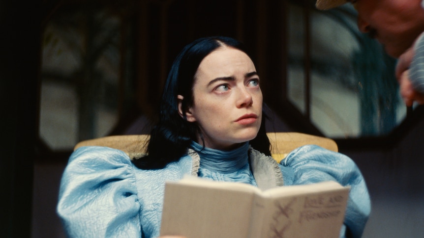 Emma Stone, as main character Bella Baxter, holds a hardcover book and looks worrying to the side.