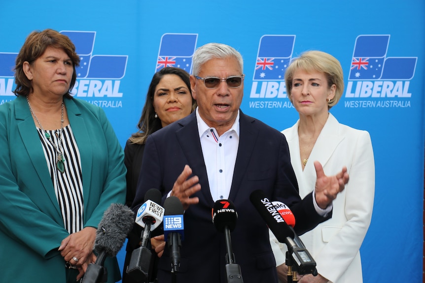 A middle-aged Indigenous man in a suit speaks to journalists, while three women stand behind him. There's a Liberal WA backdrop.
