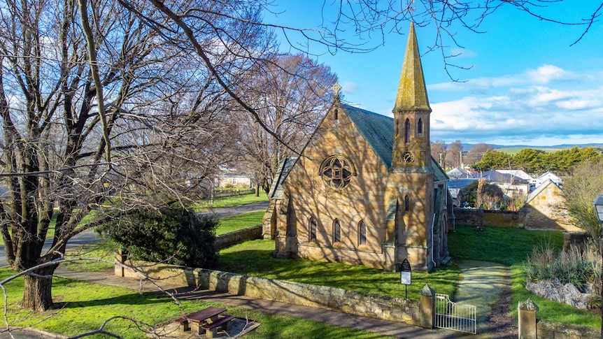 The stone church sits inside a low stone wall, with trees all around.