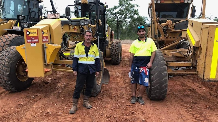 two construction workers in front of excavators