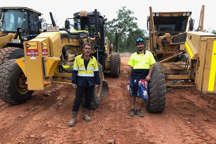 two construction workers in front of excavators