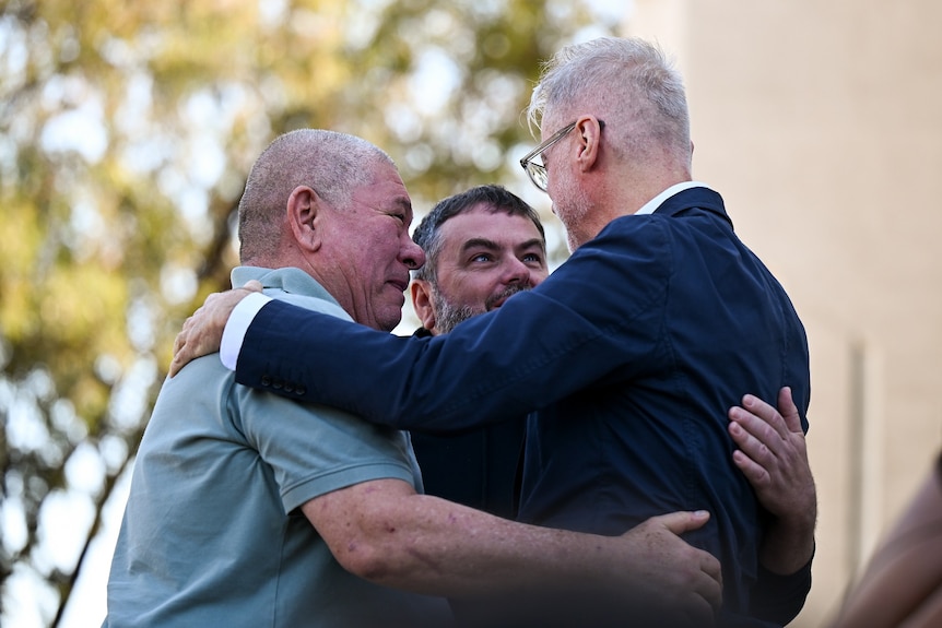 Three men embrace each other with a hug.