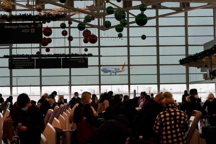 Passengers wait in an airport lounge as a plane arrives in the background.