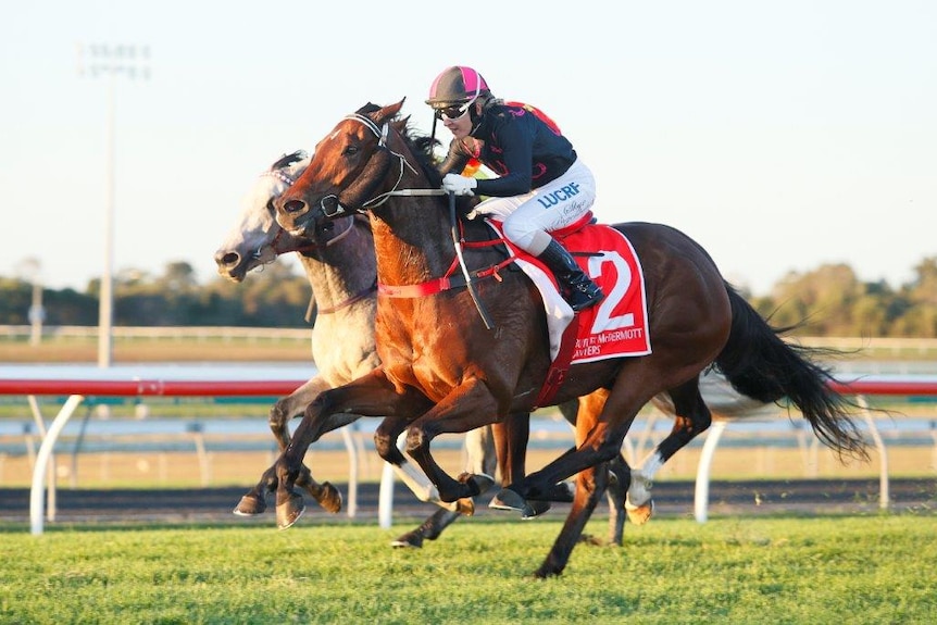 A brown horse is mid-gallop, slightly in front of another horse. Skye Bogenhuber is riding and wearing black and pink silks.