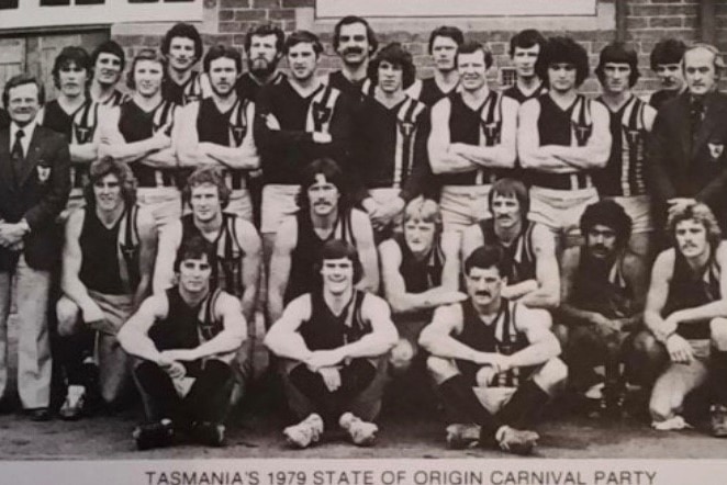 A group of men in Australian Rules outfits pose for the camera.