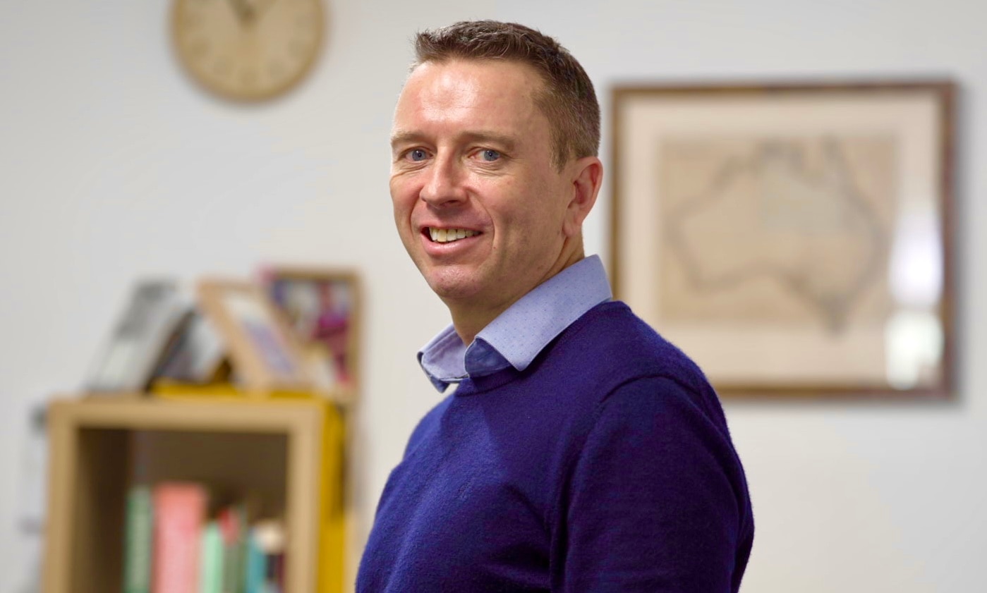 Man wearing purple jumper poses in a home office