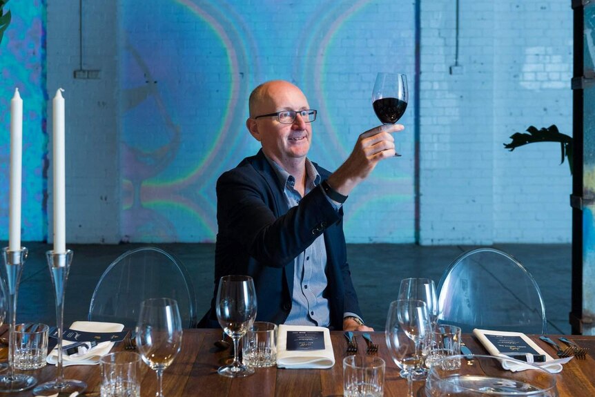 Mitchell Taylor from Taylors Wines holds a glass of red wine up to the light to check its colour.