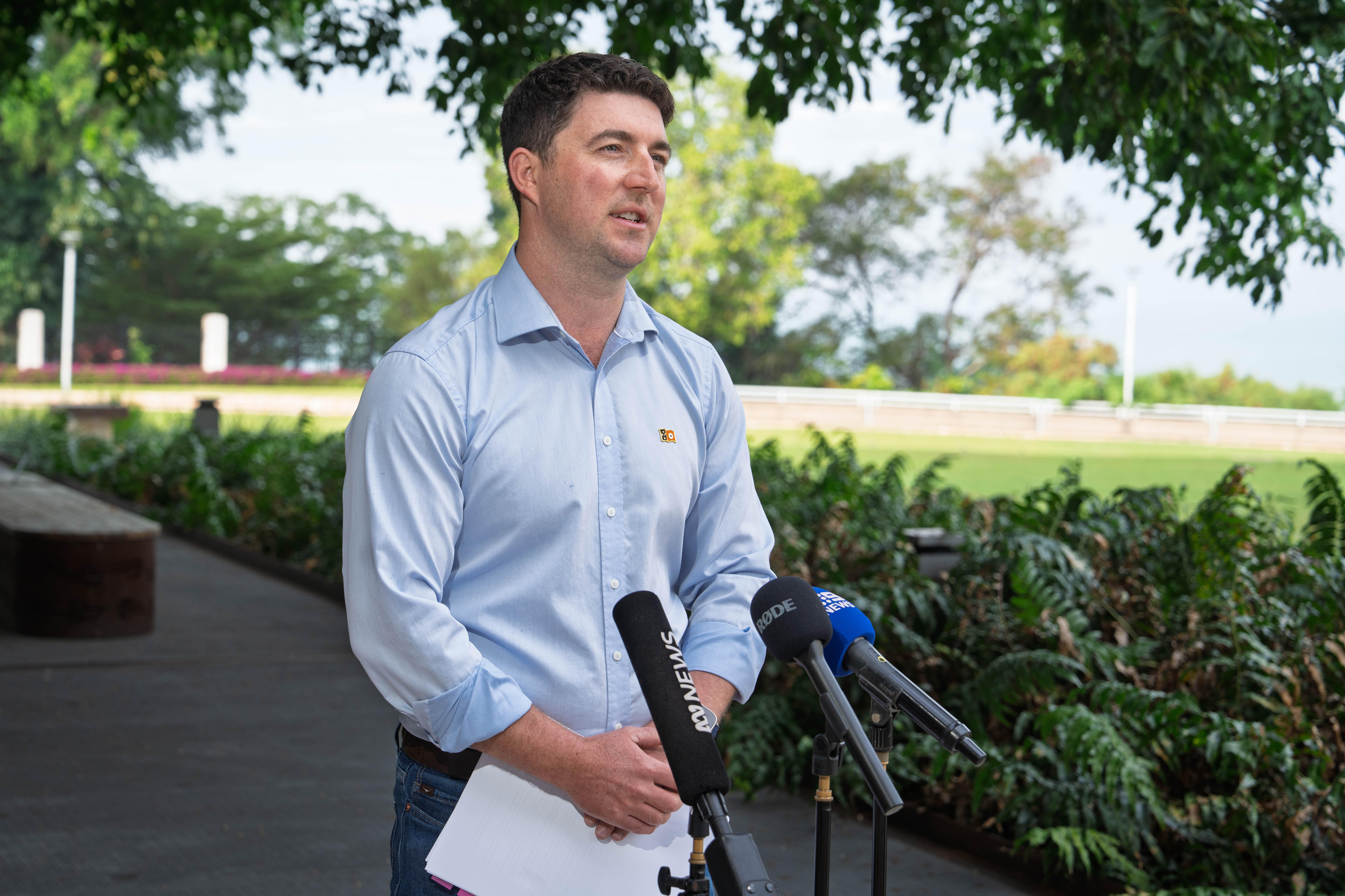 Josh Burgoyne stands outside of NT Parliament, speaking into a bank of news microphones.