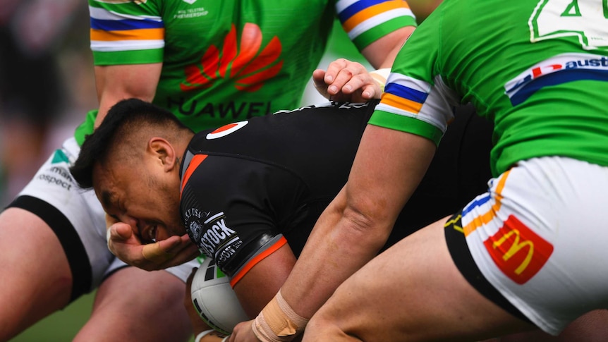 A male NRL player makes contact with the face of an opponent with his right hand as he attempts a tackle.