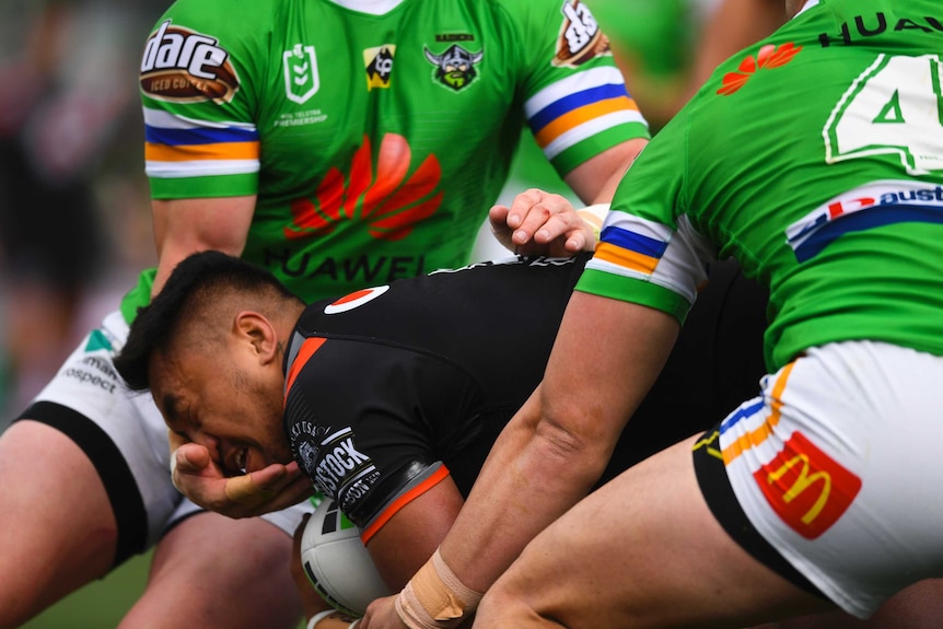 A male NRL player makes contact with the face of an opponent with his right hand as he attempts a tackle.