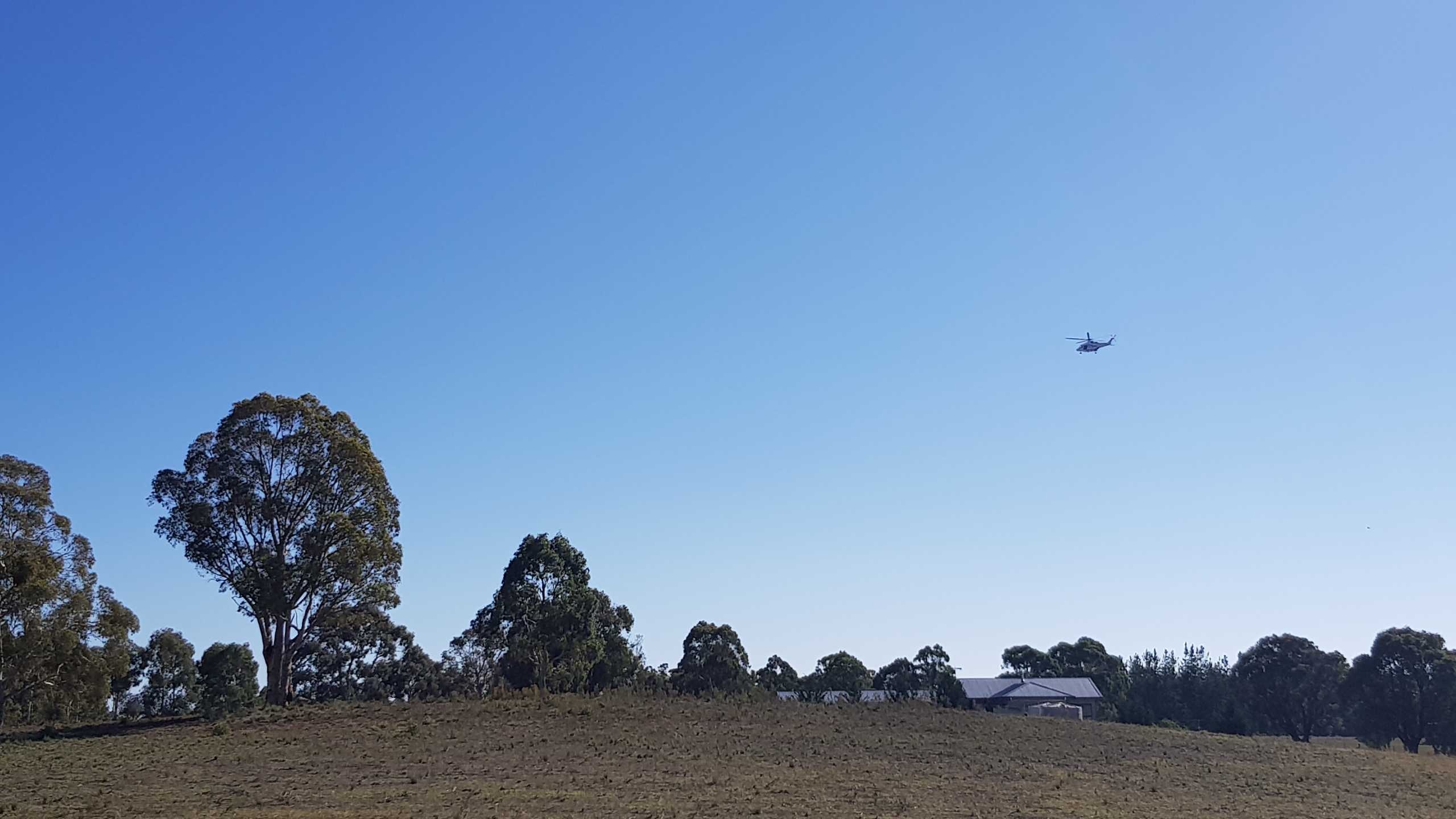 A police helicopter hovers over rural property, grass and trees.