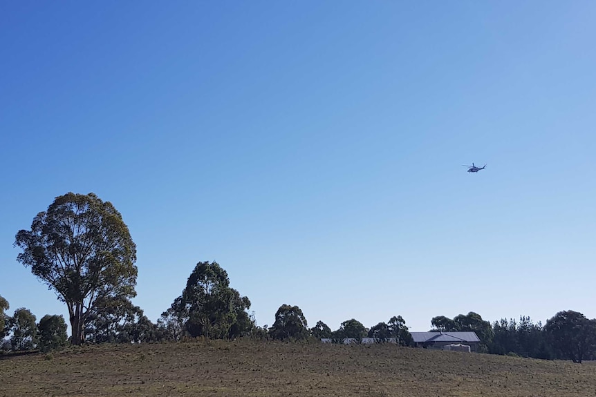 A police helicopter hovers over rural property, grass and trees.