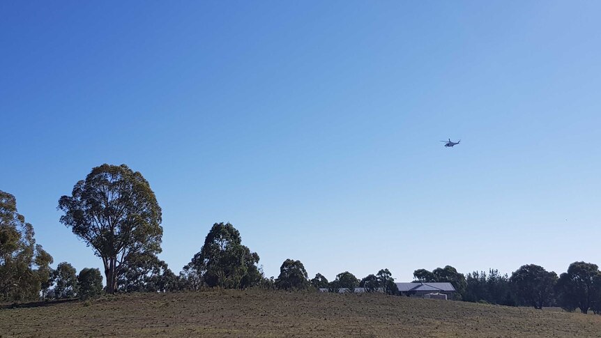 A police helicopter hovers over rural property, grass and trees.