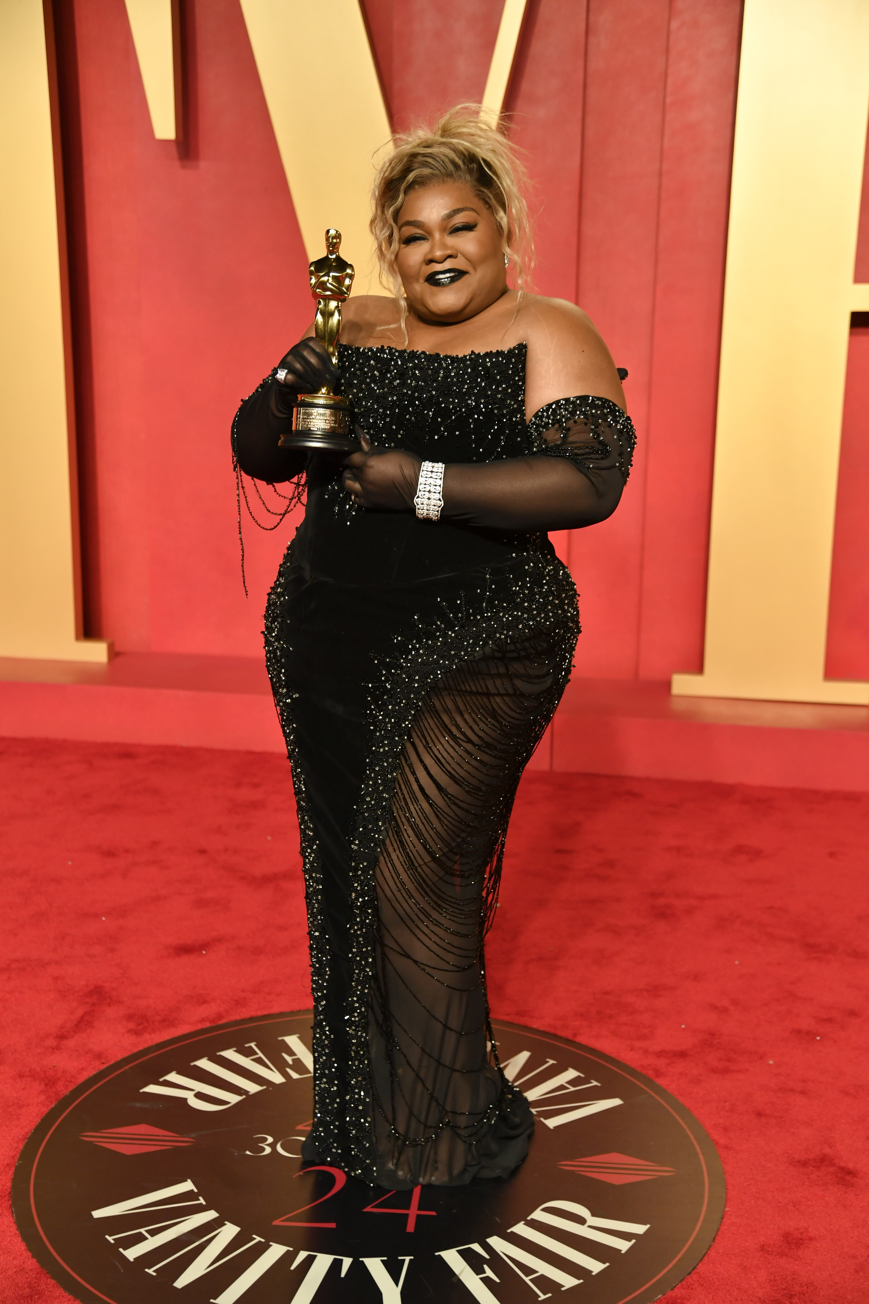 Da'Vine Joy Randolph wearing a strapless sparkly black gown with a structured bodice and draped bead strings down the skirt