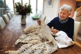 Pam Thorne sits at a table with her hand-knitted shroud made from recycled paper