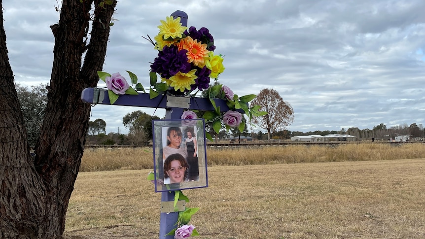 A purple cross stands near a railway track, decorated in flowers and photos of michelle