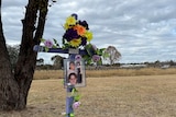 A purple cross stands near a railway track, decorated in flowers and photos of michelle