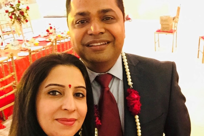 Shivani Sharma wears a red dress and takes a selfie with Vibhav Sharma, who is in a black suit.