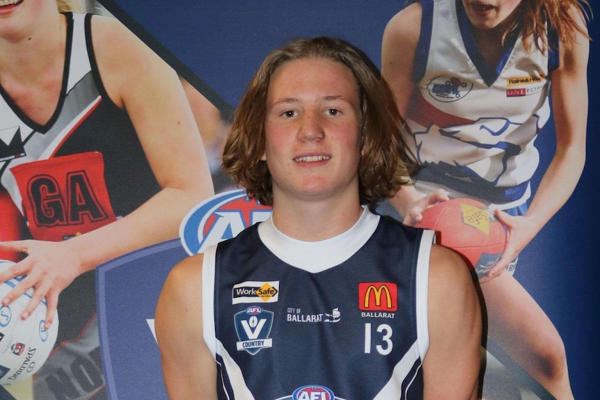 A young footballer poses for a photo in his team jumper.