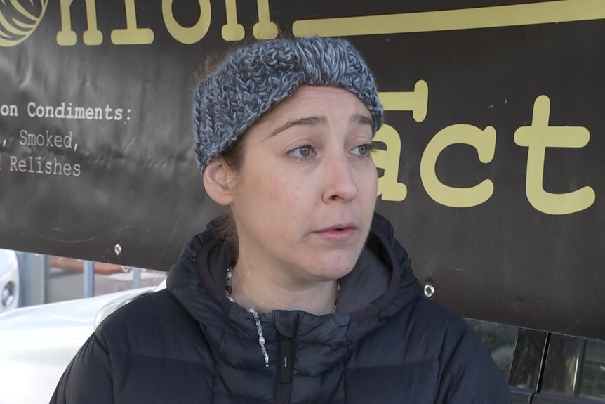 A woman wearing a black puffer jacket and grey headband looks off camera with a concerned look