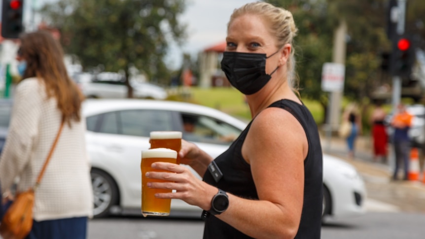Woman in black mask holds two glasses filled with beer.