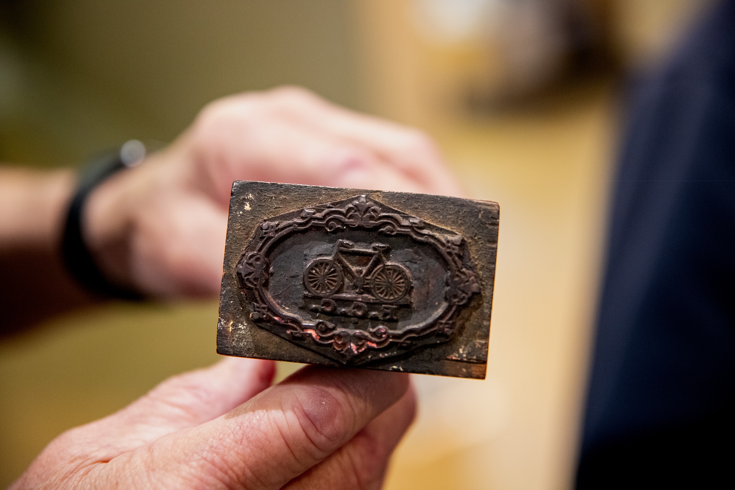 An iron stamp with a bicycle and the letters F.C.C. is held by two hands in a well lit room