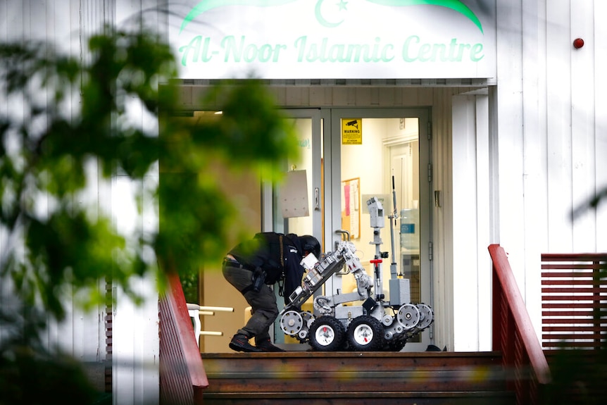 A police officer looks down at a robot outside the glass-fronted doors of al-Noor Islamic Centre.