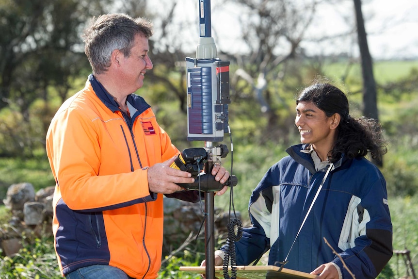 A licensed surveyor and student facing each other with surveying tripod between them.