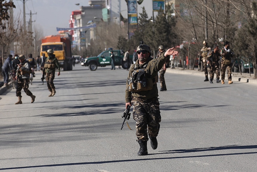 One man holds a gun in one hand and waves with the other as security arrive outside the site of a suicide attack in Kabul.