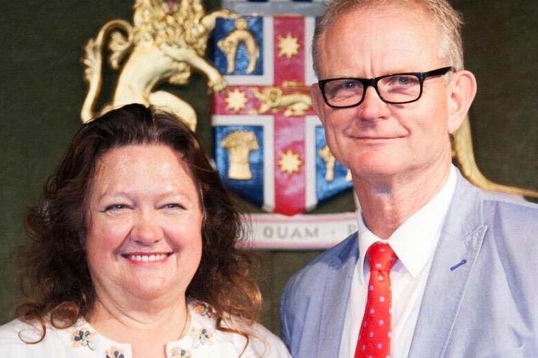 Gina Rinehart and Julian Malnic stand together and smile in front of a coat of arms.