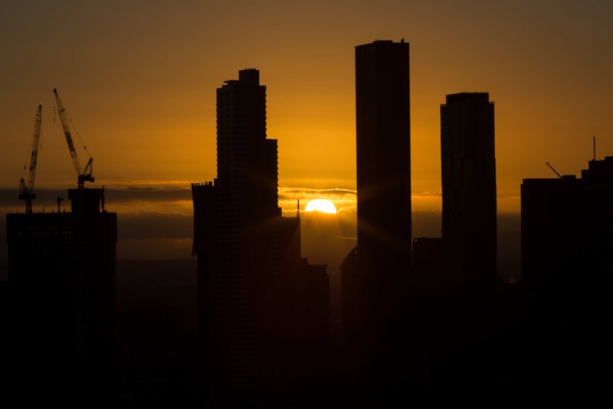 Skyscrapers in silhouette against a golden sky as the sun rises.