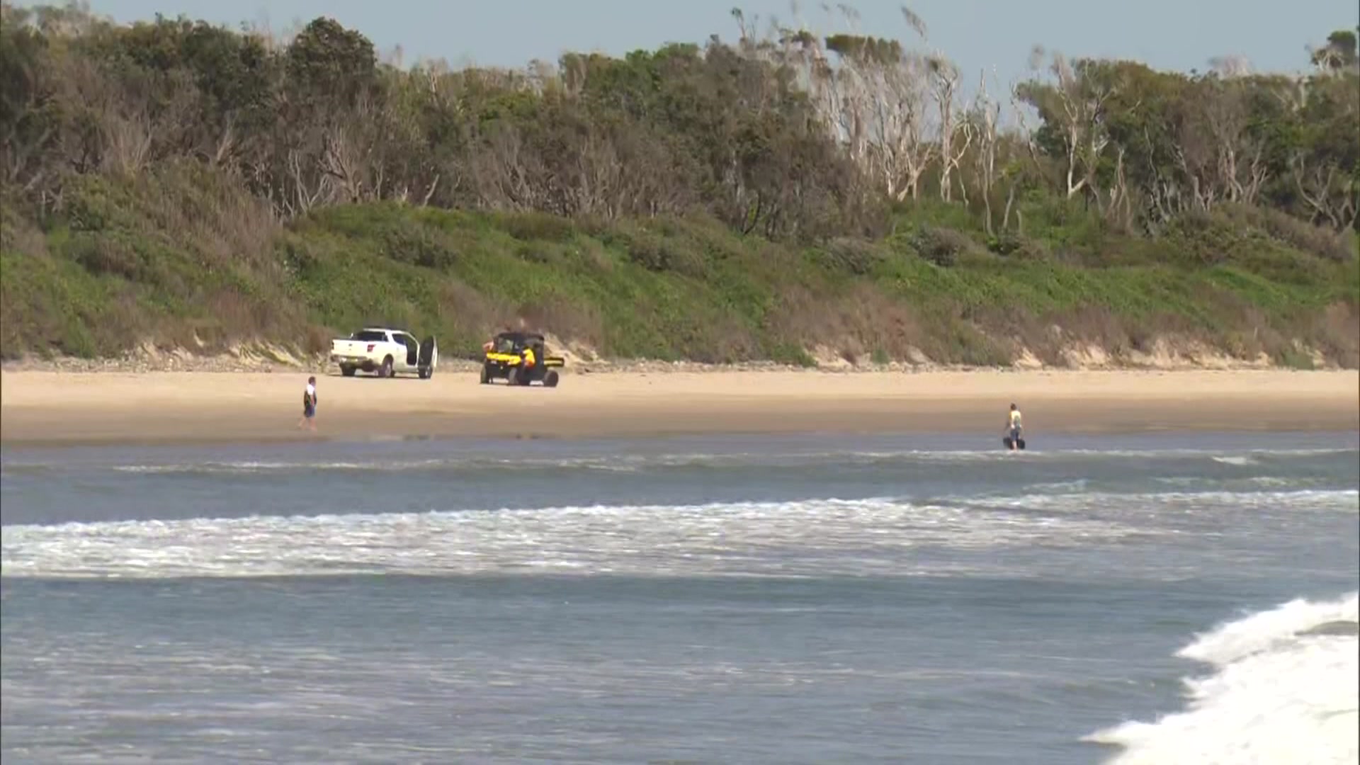 Una ute y un buggy en una playa bordeada por un promontorio bajo y accidentado.