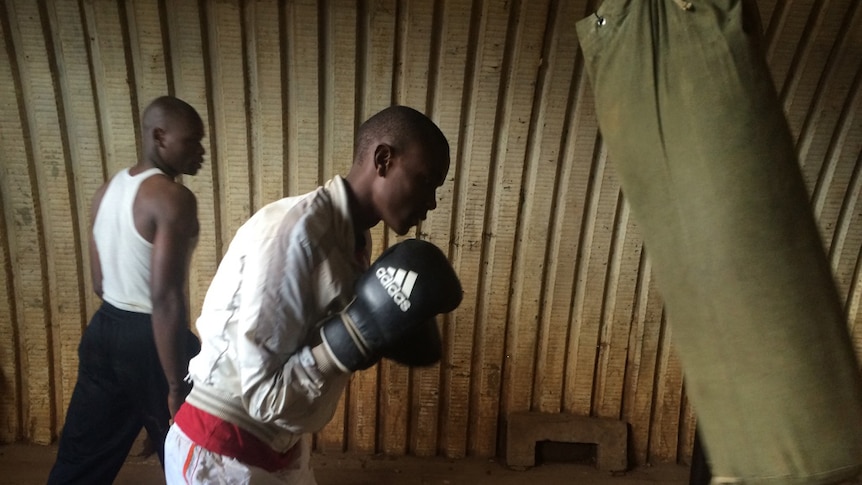 A young man wearing boxing gloves punches a swinging boxing bag.