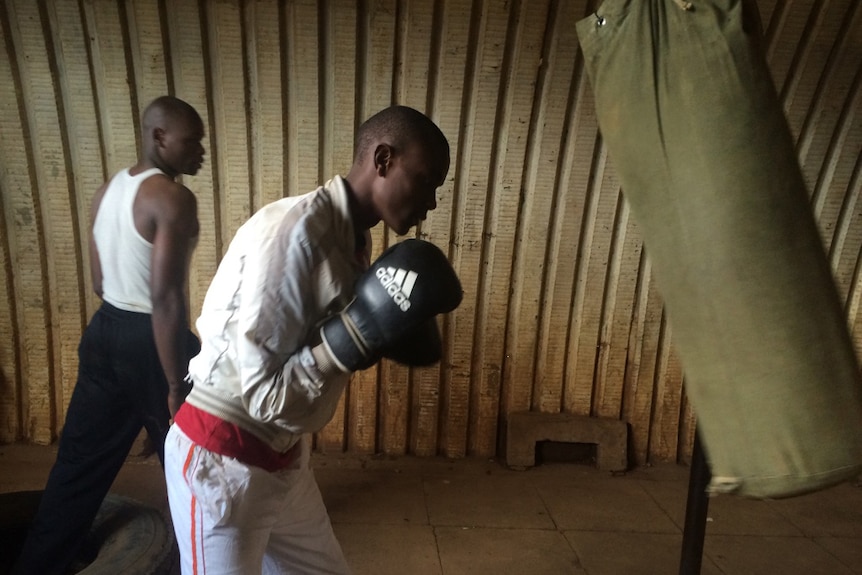 A young man wearing boxing gloves punches a swinging boxing bag.