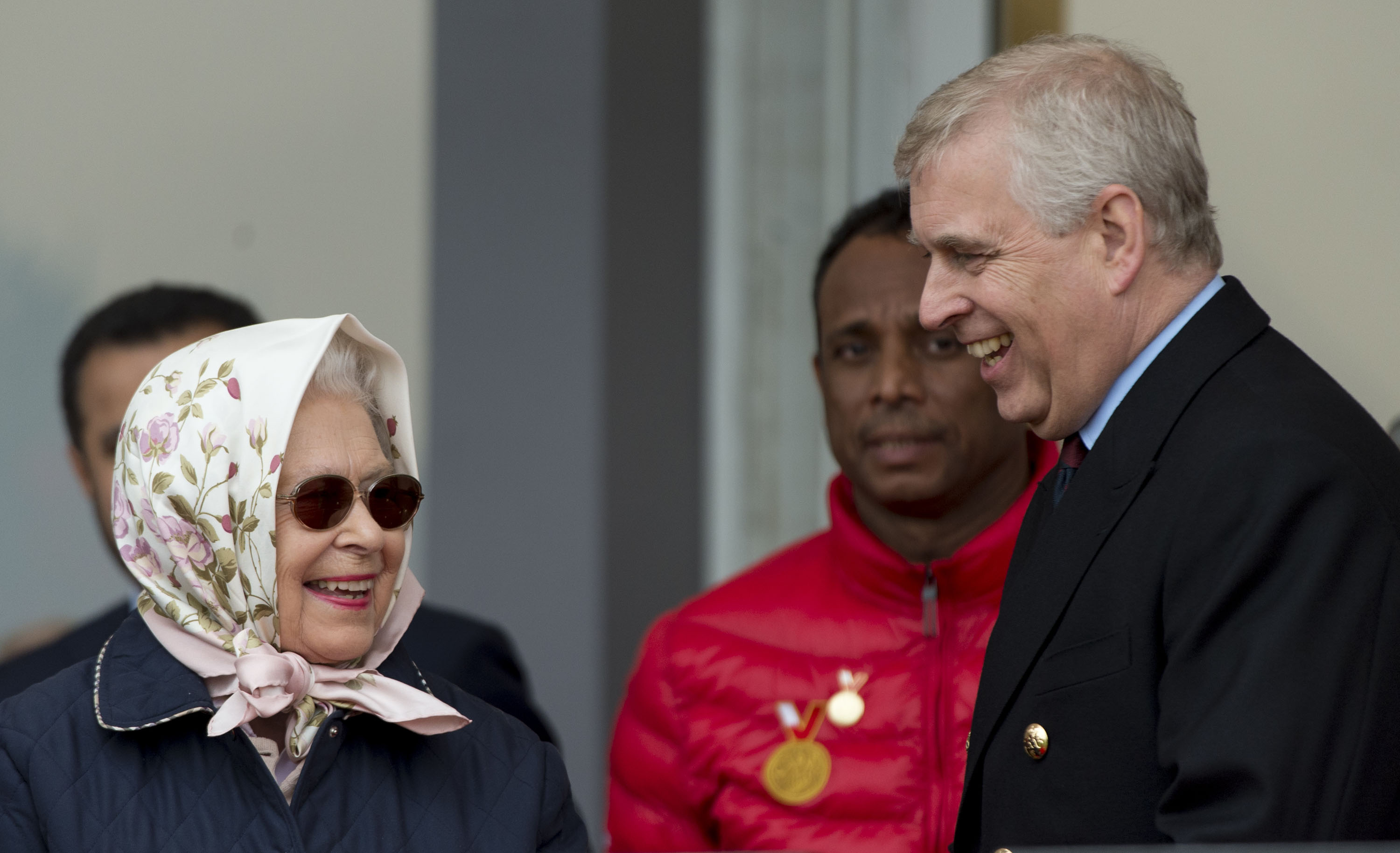 A woman in a headscarf and sunnies laughs with a man in a suit