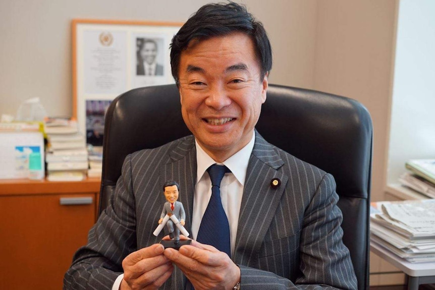MP Shigefumo Matsuzawa holds a small figurine of himself snapping a cigarette.