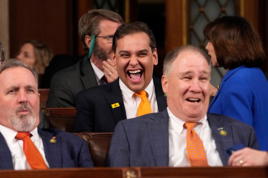 George Santos sit in Congress smiling.