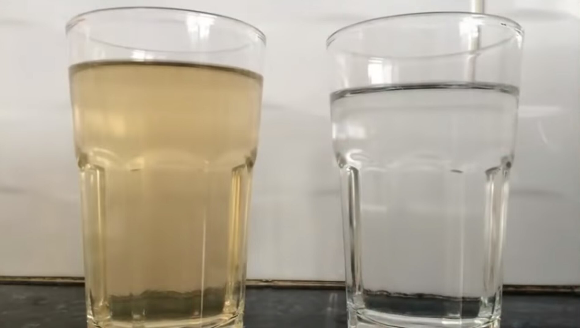 Two glasses sit side by side, one with brown water in it and the other with clear water.