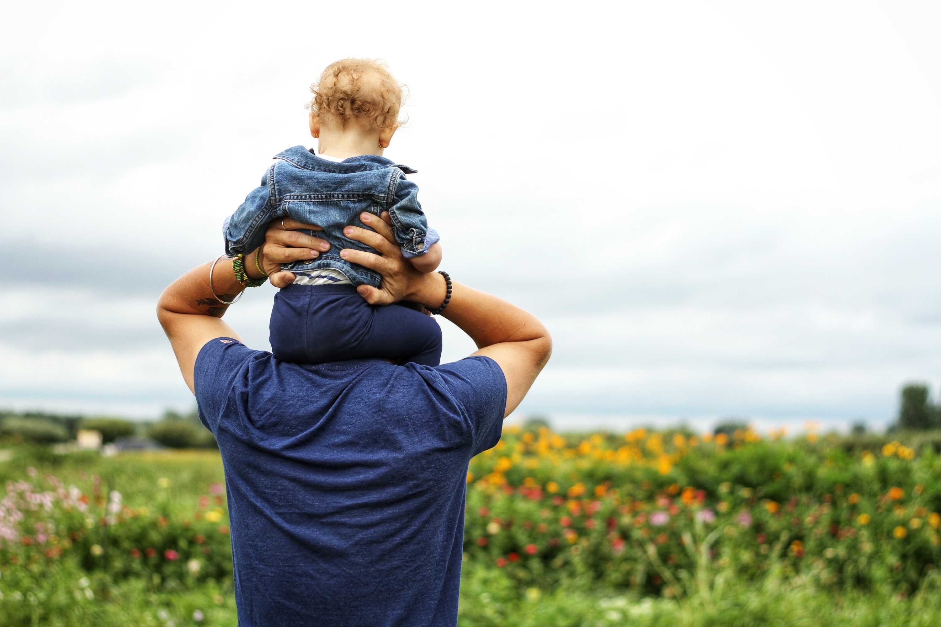 Man with a toddler on his shoulders looks toward the ocean for a story about male infertility and sperm count