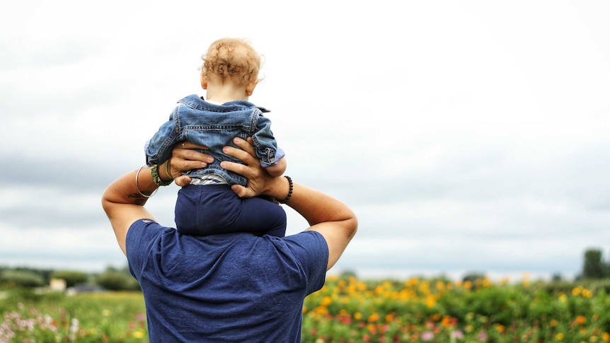 Man with a toddler on his shoulders looks toward the ocean for a story about male infertility and sperm count