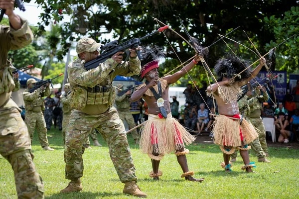 soldiers with guns alongside dancers in traditional Torres Strait dress with bows and arrows pointed at the sky