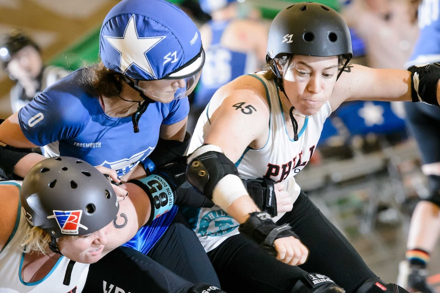 A roller skating woman in blue team colours is sandwiched by two players in white.