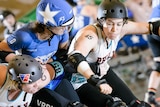 A roller skating woman in blue team colours is sandwiched by two players in white.