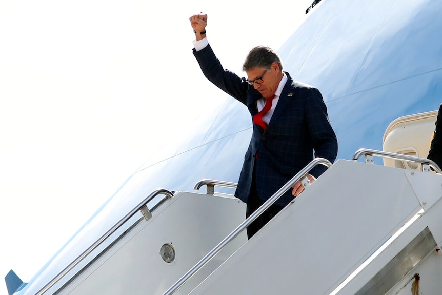 On a staircase leading up to Air Force One, US Energy Secretary Rick Perry holds his first in the air as he wears a dark suit.